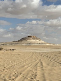 a sand dune in the desert with clouds in the sky