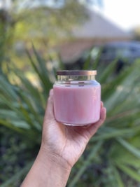 a hand holding a pink candle in front of a palm tree