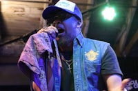 a man in a vest and hat singing into a microphone