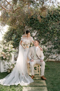 a bride and groom sitting on a chair in a garden