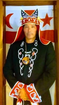 a man in a traditional costume posing in front of a flag