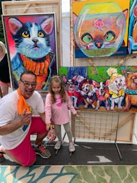 a man and a little girl standing in front of a display of paintings