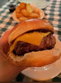 a person is holding a cheeseburger with fries on a table