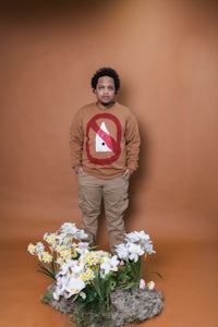 a man standing in front of flowers in a brown sweater