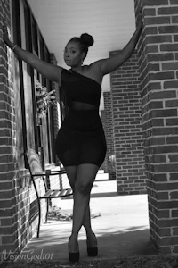 a black woman in a black dress leaning against a brick wall