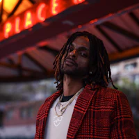 a man with dreadlocks standing in front of a neon sign