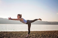 a woman doing yoga on a beach near a lake