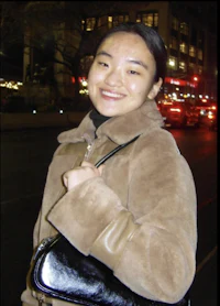 a woman in a brown coat holding a black purse