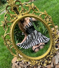 a girl in a black and white striped dress is posing in front of a gold mirror