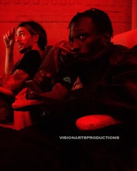 two men sitting on a couch in front of a red light