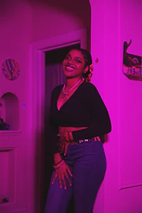 a woman in a black top and jeans standing in a pink room