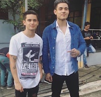 two men standing next to each other in front of a camera