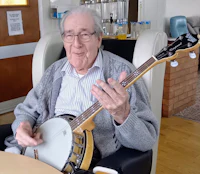 an elderly man playing a banjo in a chair
