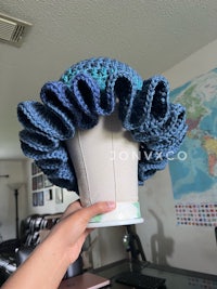 a person is holding a crocheted blue ruffled hat