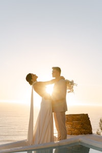 a bride and groom standing in front of a pool at sunset