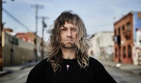 a man with long hair standing in a street