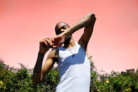 a man in a white tank top posing in front of bushes