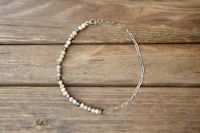 a necklace with silver beads and a chain on a wooden table