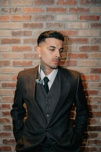 a man in a suit leaning against a brick wall