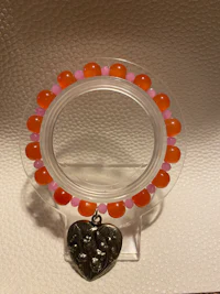 a bracelet with orange and pink beads and a heart shaped charm