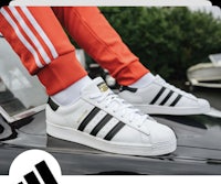 a man is standing on top of a car wearing a pair of adidas superstars