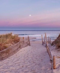 a sand path leading to the beach at sunset