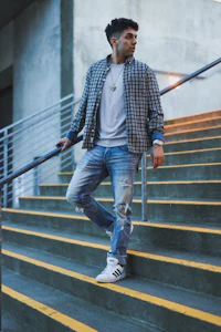 a man standing on stairs wearing a plaid jacket and jeans