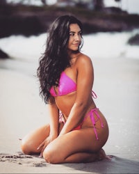 a woman in a pink bikini sitting on the beach