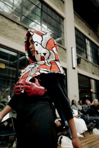 a woman wearing a hoodie and a scarf on a runway