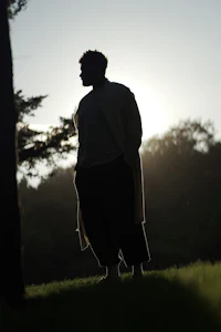 a silhouette of a man standing in a field at sunset