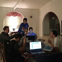 a group of people sitting around a table with laptops