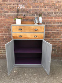 a purple painted cabinet with two drawers and a potted plant