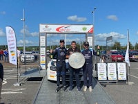 three men standing next to a rally car with a trophy