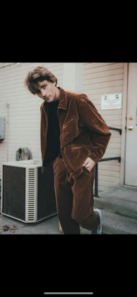a young man in a brown jacket standing next to an air conditioner