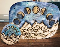 a piece of wood with a moon and mountains on it