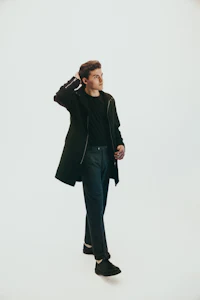 a young man in a black coat standing on a white background