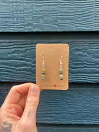a person holding up a card with green and blue beads on it