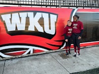 two softball players standing in front of a wall with a wku logo