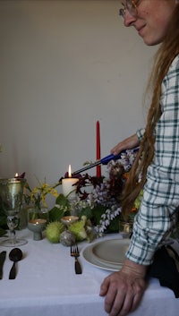 a woman is setting a table with flowers and utensils