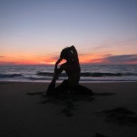 a woman doing yoga on the beach at sunset
