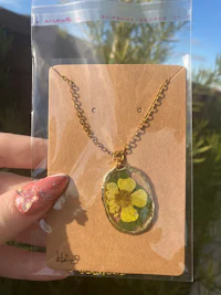 a person holding a necklace with a yellow flower on it