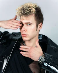 a young man in a black leather jacket posing with his hands on his face
