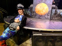 a man posing in front of a stage with a moon behind him