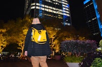 a person in a yellow backpack standing in front of tall buildings at night