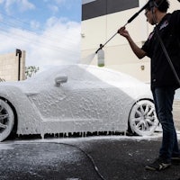 a man is washing a white car with a hose