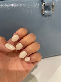 a hand holding a blue handbag with white nails