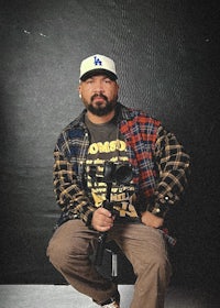 a man in a plaid shirt and hat sitting on a stool
