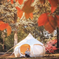 a woman sits in a white yurt in the autumn leaves