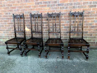 a set of four wooden chairs against a brick wall