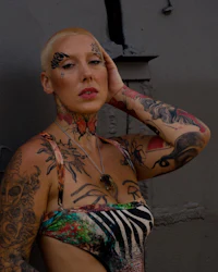 a woman with tattoos leaning against a wall